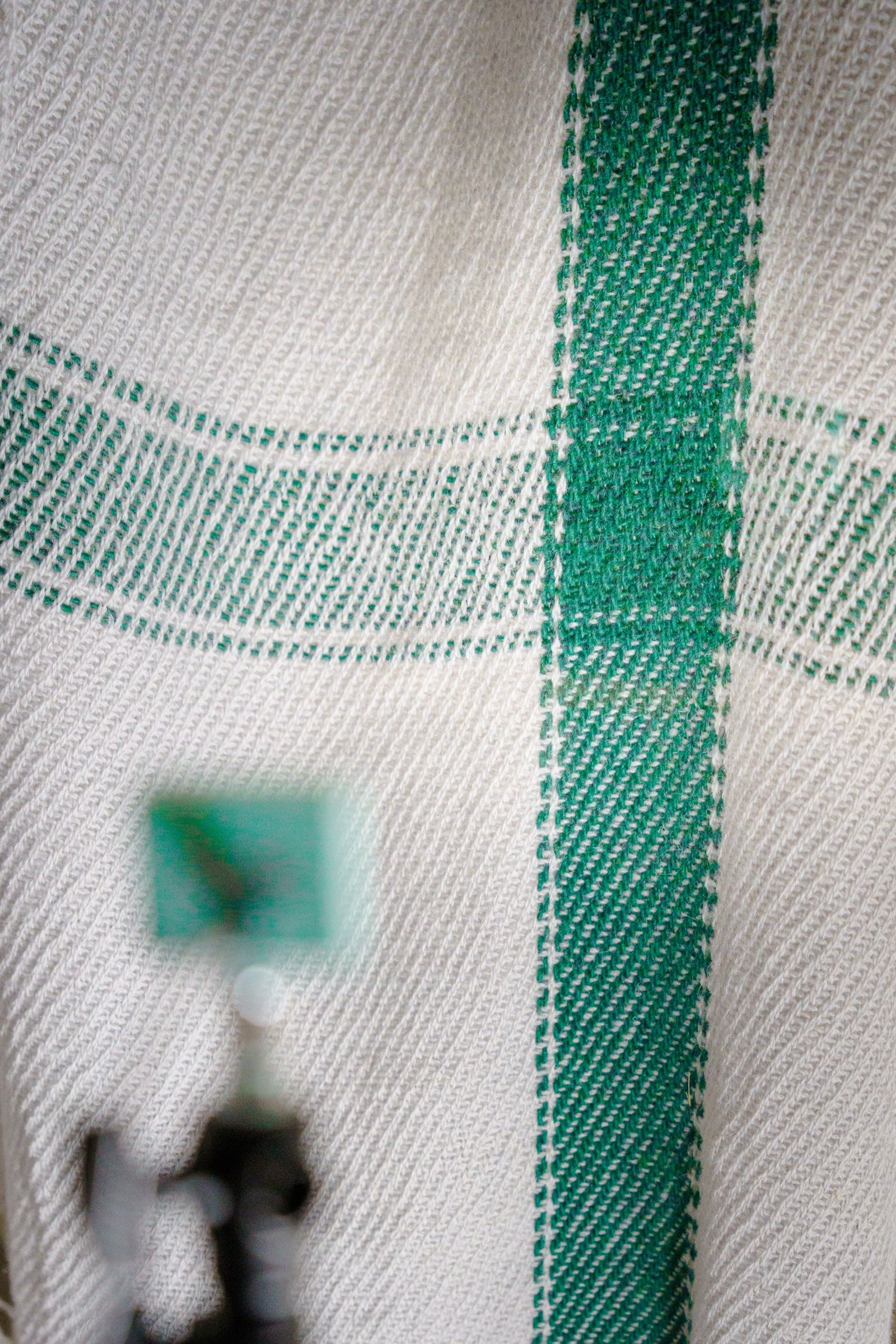 A close-up of the twill weave where the green stripes cross, the camera soft and out of focus in front